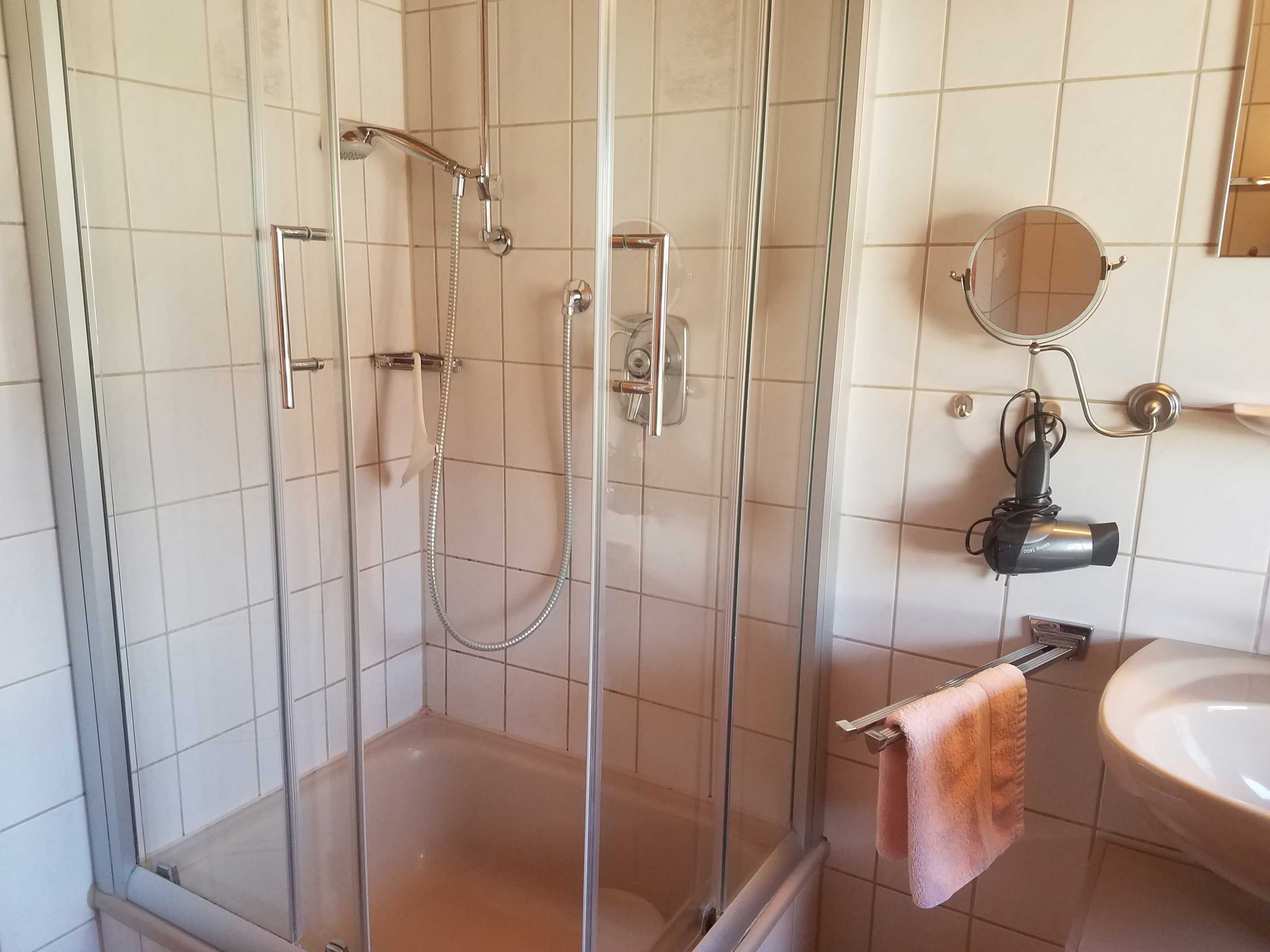 A bathroom with a glass-enclosed shower, a sink, a towel rack, and a hairdryer.