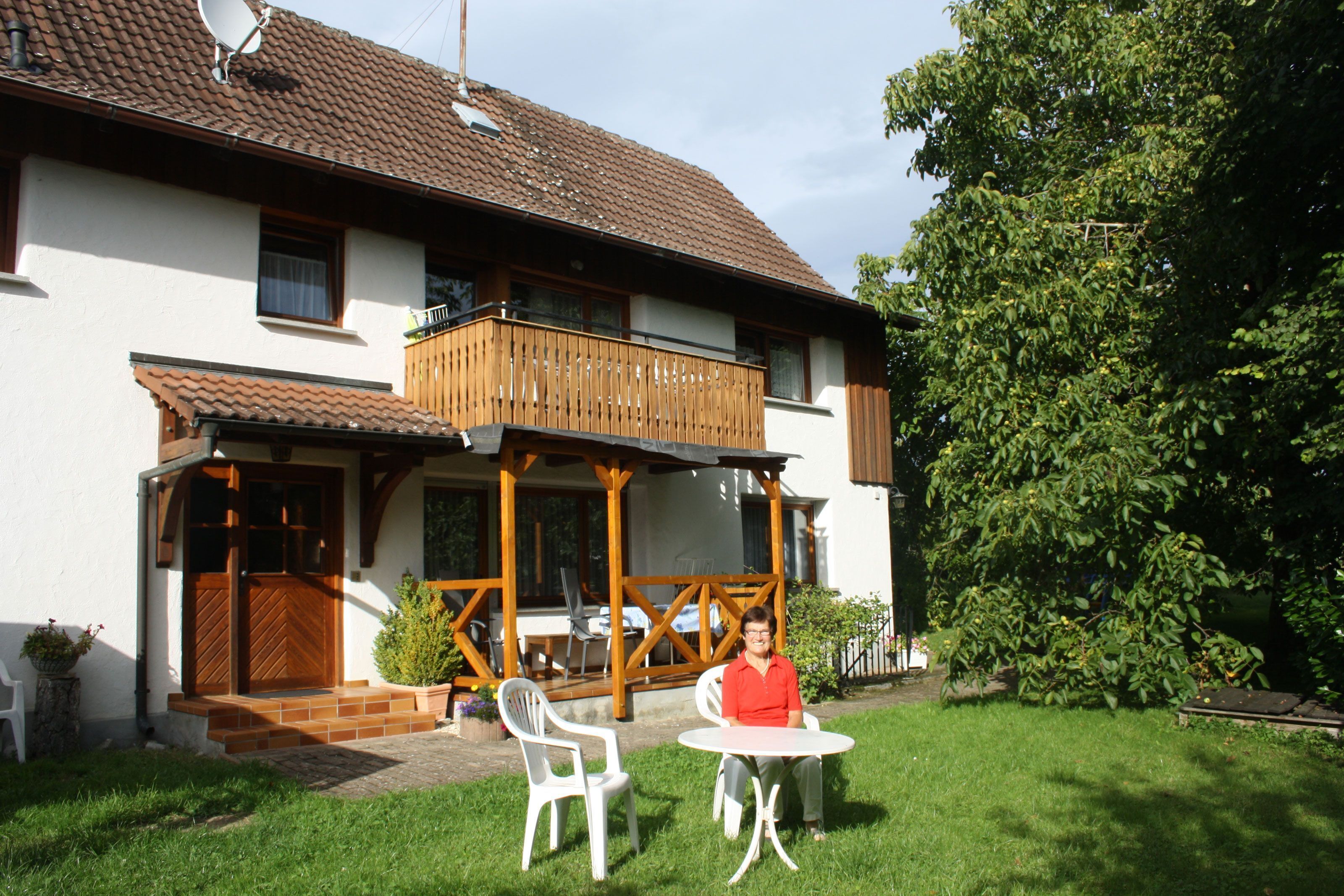 Ein zweistöckiges Haus mit Balkon, einer Terrasse mit Stühlen und einem kleinen Garten.