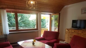 A living room with a wooden ceiling, a TV on a wooden cabinet, and a view of greenery outside.