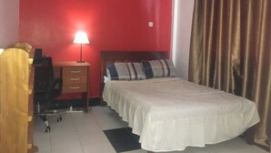 Une chambre à coucher avec un lit, une table de chevet avec une lampe, un bureau avec une chaise et un rideau.