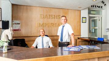 Een receptiebalie bij Daish's Imperial met twee medewerkers, een houten wand en een bord met daarop 'lounges'.