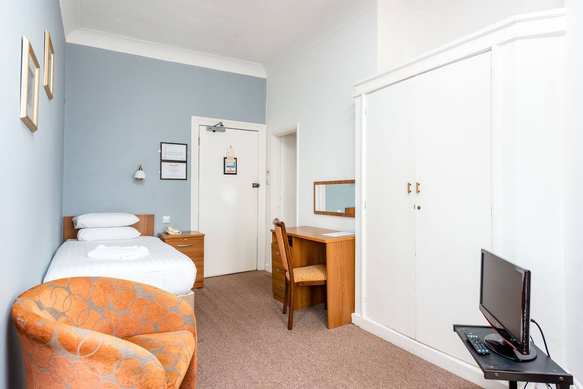 A hotel room with a bed, a desk, a chair, a TV, and a wardrobe.