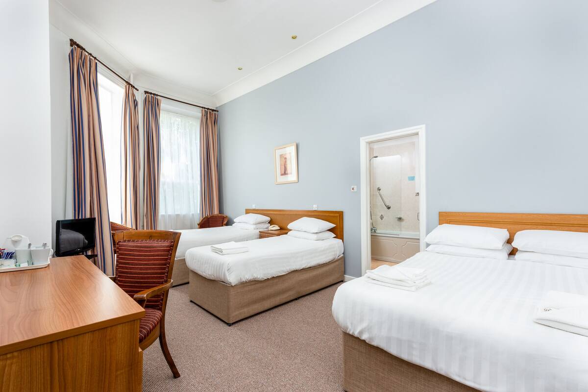 A hotel room with two beds, a desk, a chair, and a shower area.
