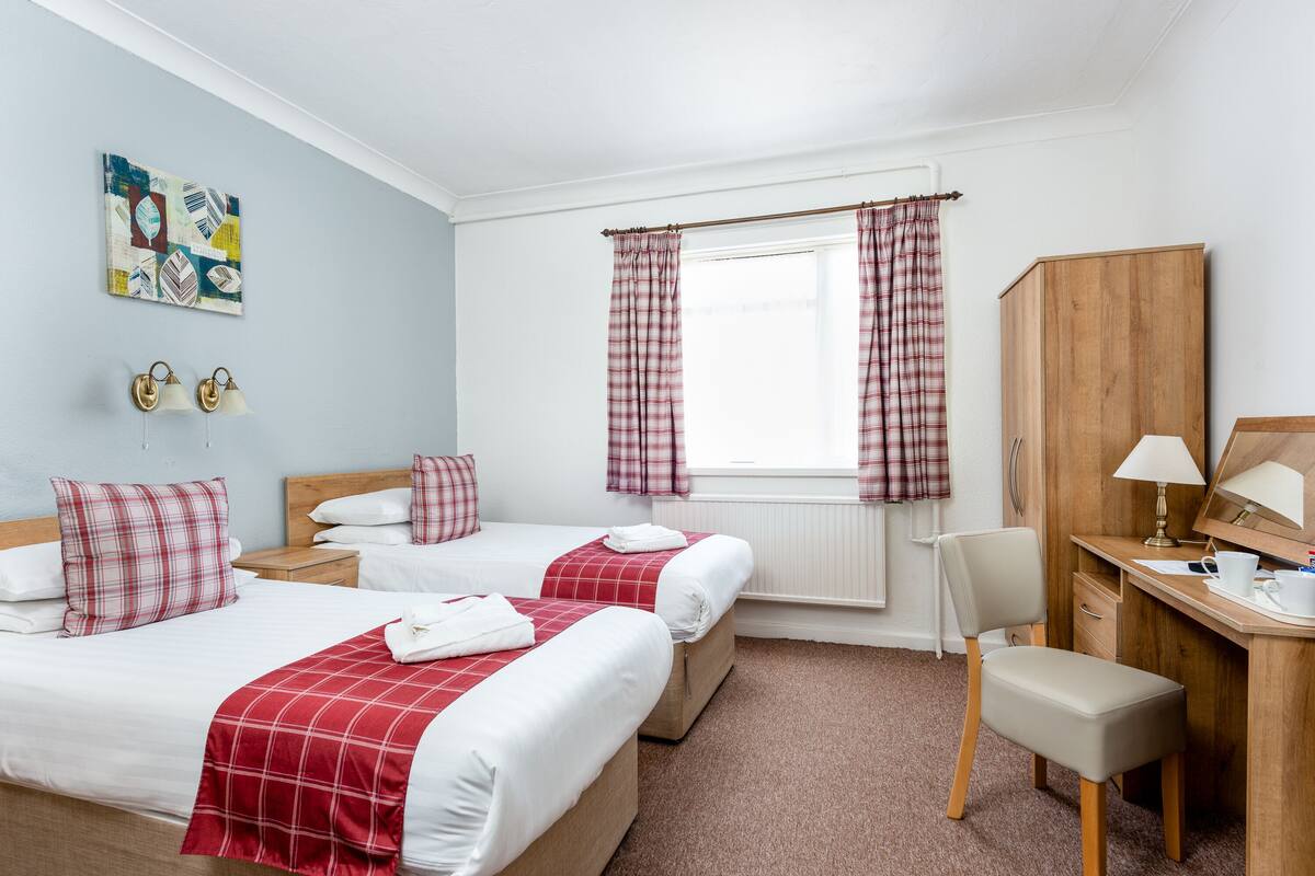 A hotel room with two beds, a desk, a chair, a wardrobe, and a window with curtains.