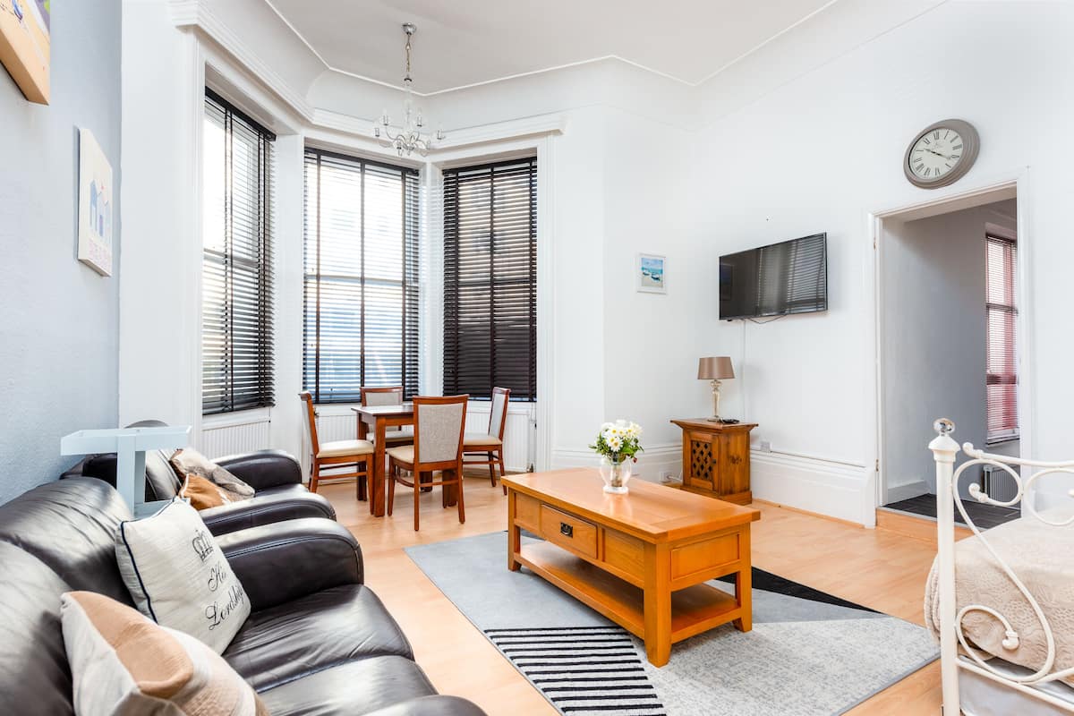 A living room with a sofa, a wooden coffee table, a TV, and a dining area with chairs and a table.