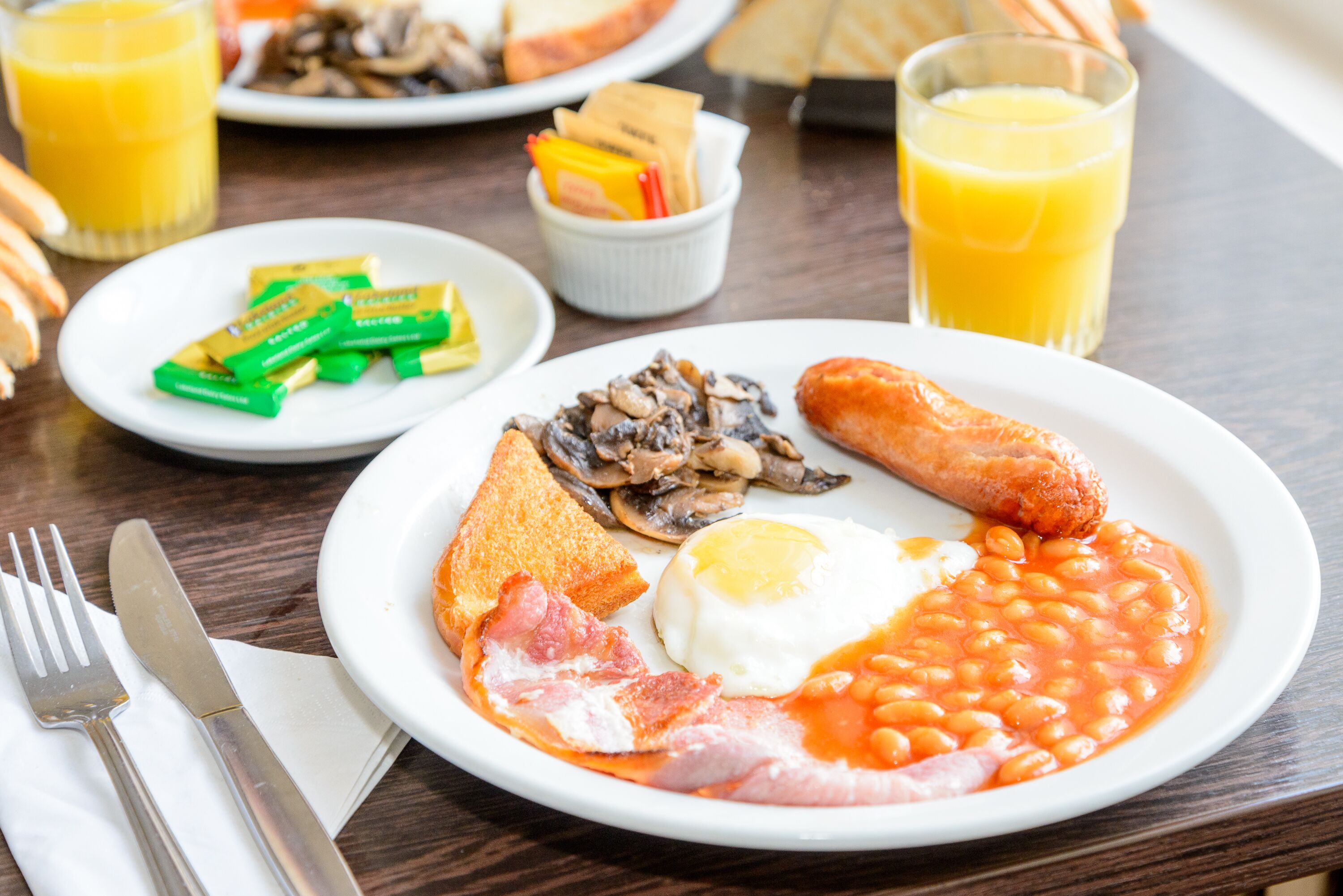 A breakfast plate with eggs, beans, bacon, mushrooms, and sausage.