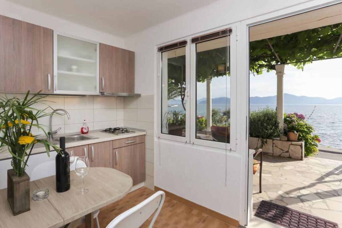 A kitchen with a view of the sea, a dining table with a vase of flowers, and a wine glass.