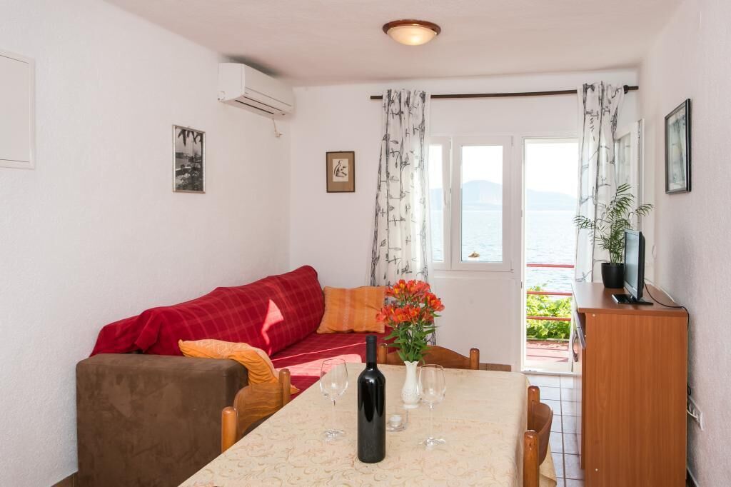 A cozy room with a dining table, a red sofa, a TV, and a view of the sea.