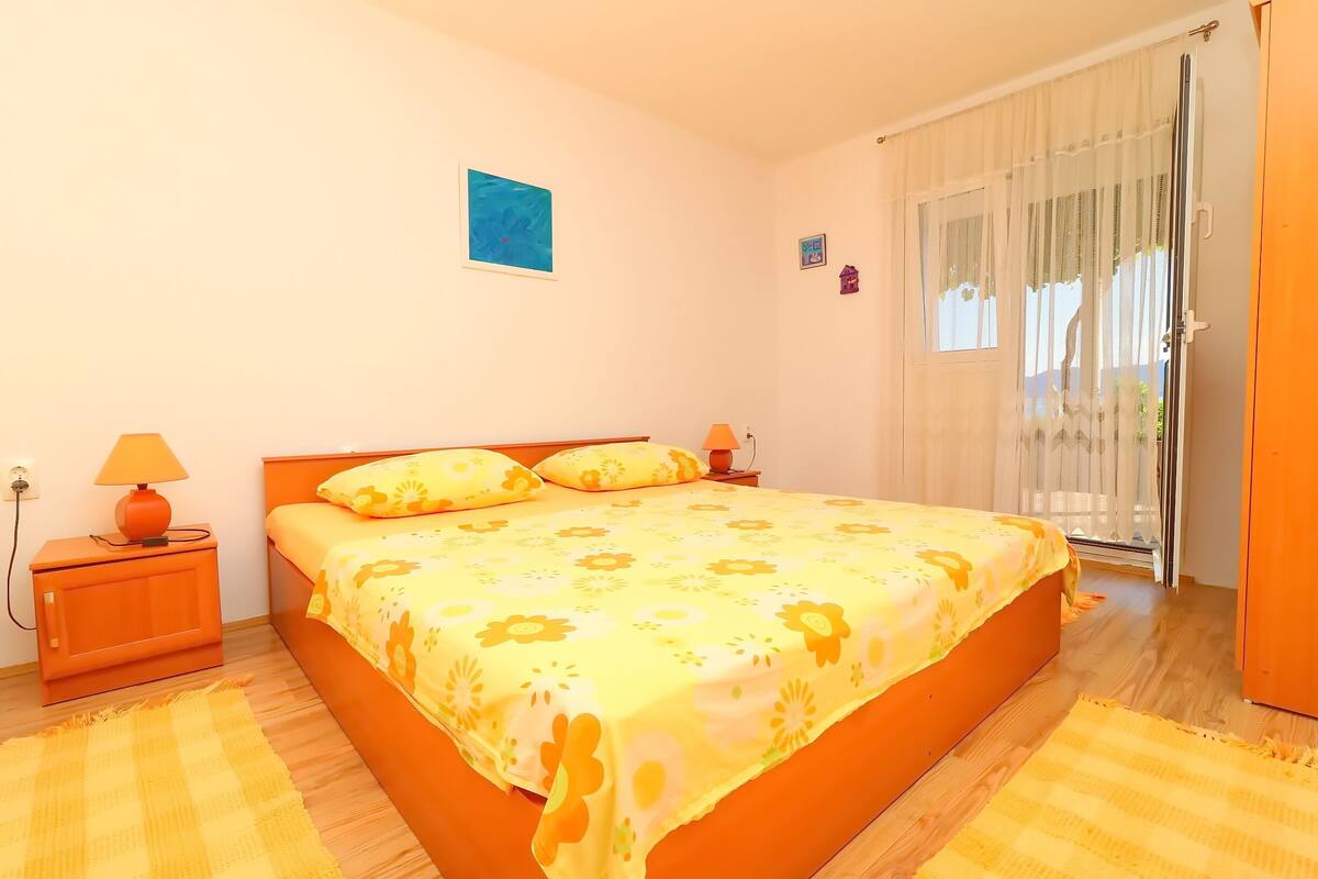 A bedroom with a large bed, two bedside tables, a nightstand, a window with curtains, and a door.
