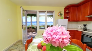 A dining area with a table set for two, a fruit bowl, and a pink hydrangea. - Apartments Stipo (Janjina)