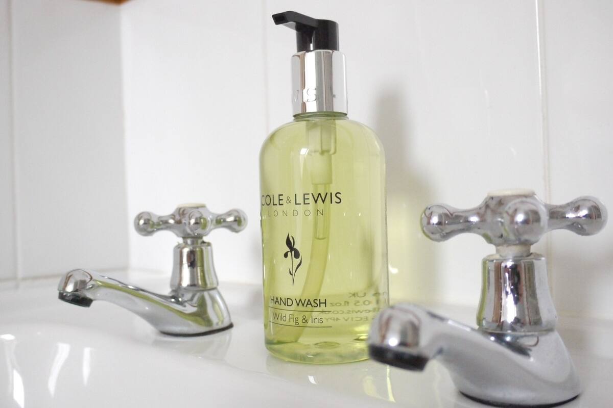 A bathroom with a hand wash bottle labeled 'COLE & LEWIS LONDON' and two classic-style faucets.