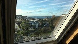 A view through a window of a residential area with houses, a stone wall, and a clear sky. - Appletree (Isles of Scilly)