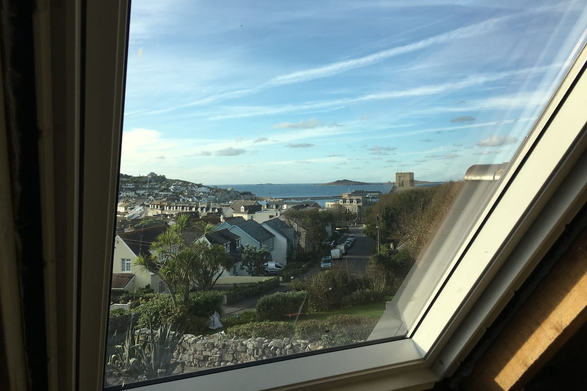A view through a window of a residential area with houses, a stone wall, and a clear sky.
