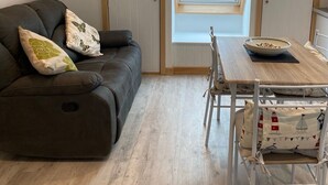 A cozy loft bedroom with a dark leather sofa, a wooden dining table, and a skylight window. - Appletree (Isles of Scilly)