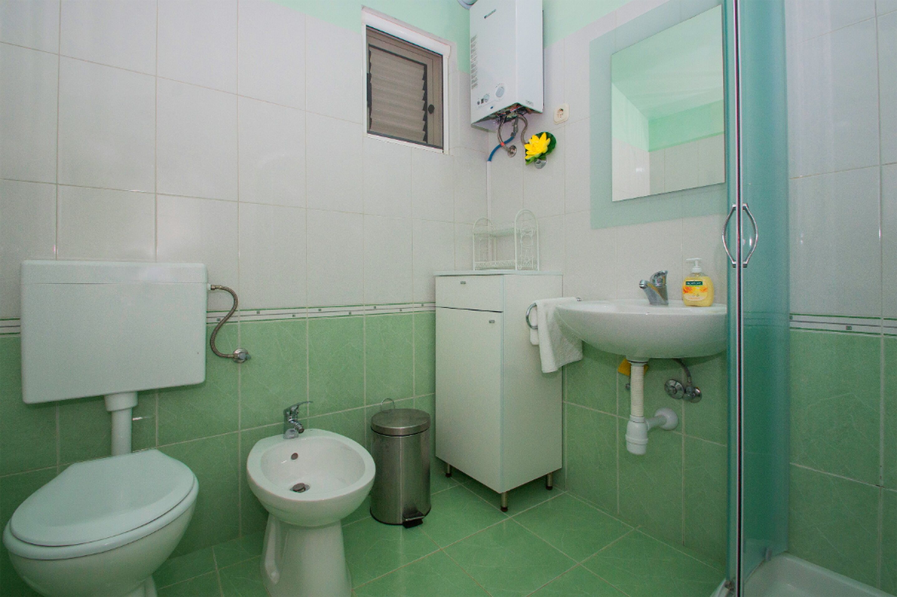 A bathroom with a toilet, bidet, sink, and a trash bin.