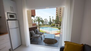 A modern kitchen with a built-in microwave and refrigerator, a balcony with a pool view, and a seating area with a yellow cushion. - New front line beach apartment with swimming pool, A/C and WIFI (Almuñecar)