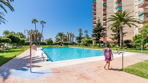 A swimming pool with a tiled deck, surrounded by palm trees and a multi-story building. - New front line beach apartment with swimming pool, A/C and WIFI (Almuñecar)