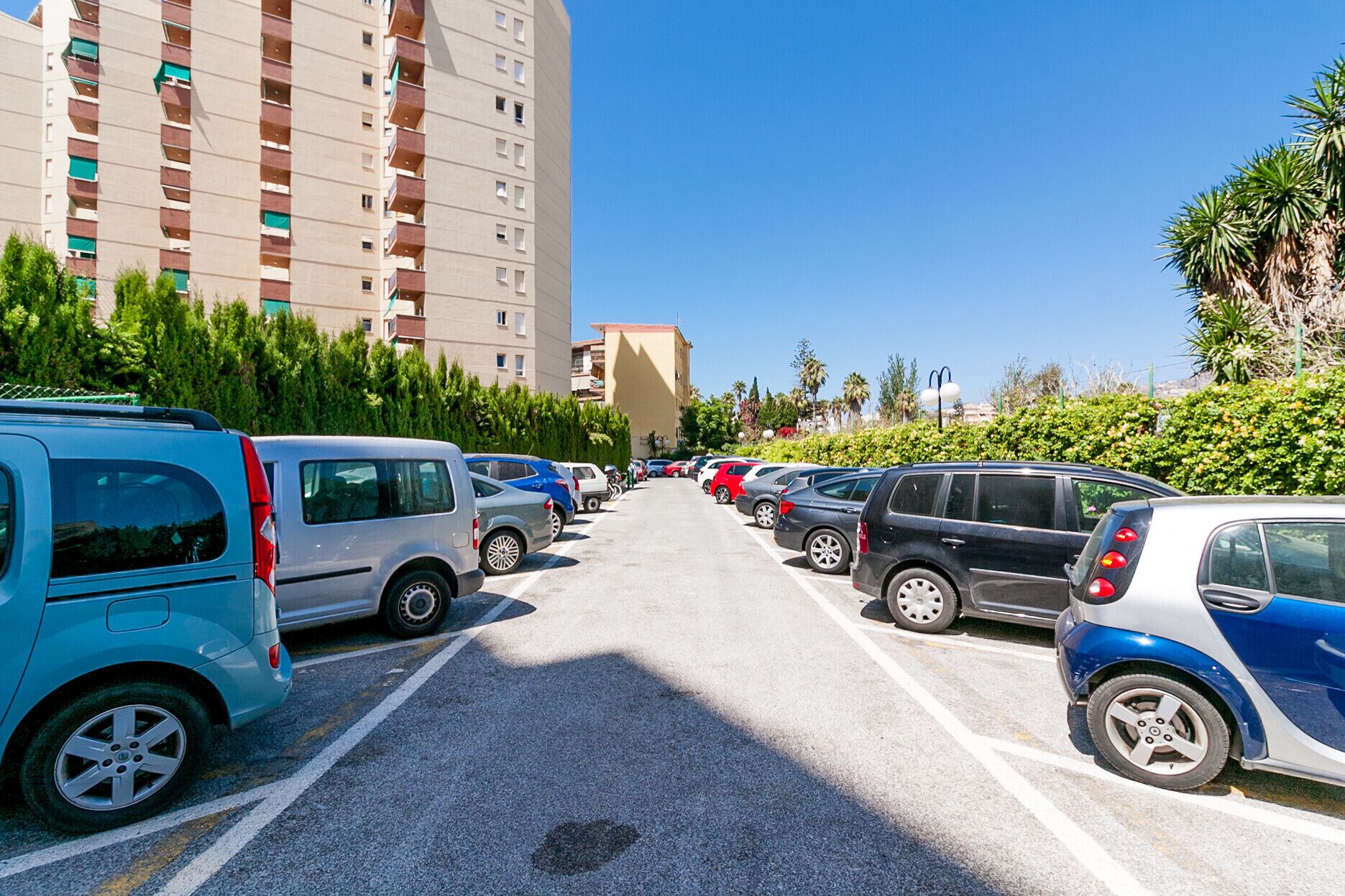 Un estacionamiento con varios automóviles y un edificio alto al fondo.