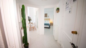 A hallway leading to a bedroom with a bed, a desk, and chairs. There is a cactus in a pot on the left and a door with a sign on the right. - New front line beach apartment with swimming pool, A/C and WIFI (Almuñecar)