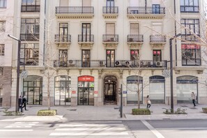 Un immeuble à plusieurs étages doté d’une entrée imposante, de grandes fenêtres et d’une enseigne rouge indiquant qu’il s’agit d’un commerce.