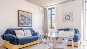 A modern living room with a blue sofa, a glass dining table, and clear chairs. There is a framed picture on the wall and a geometric art piece above the window. - Central apartment with parking to discover Granada (Granada)