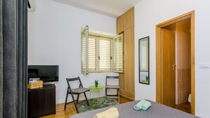 A bedroom with a bed, a desk with a TV, two chairs, a small table with a plant, and a wooden wardrobe. - The Point Room (Dubrovnik)