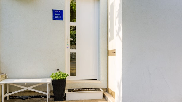 A white door with a blue sign above it, a white bench, and a potted plant on the steps. - The Point Room (Dubrovnik)
