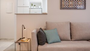 Een woonkamer met een beige bank, een bijzettafeltje met een lamp en een kunstwerk in een lijst aan de muur.