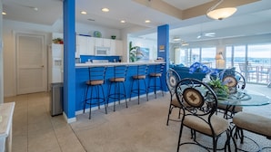 A modern kitchen with blue accents, a bar area with stools, and a dining area with a glass table and chairs.