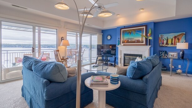 A living room with a blue sofa, a coffee table, and a TV. There is a fireplace and a painting on the wall.