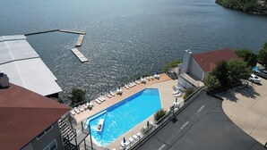 A swimming pool with a view of a lake, surrounded by buildings and a parking area.