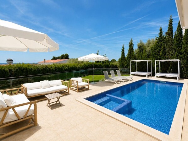 Une piscine rectangulaire dont le bord est recouvert de carreaux, entourée de chaises longues et de parasols.
