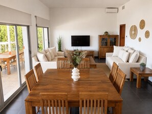 A modern living room with a wooden dining table, sofas, a TV, and a large window. - VILLA ORQUIDEA DELUXE VILLA ❤️ SEA VIEWS 2 POOLS &  JACUZZI ❤️ (San Jaime Mediterráneo)