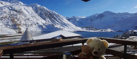 A snowy mountain landscape with a lake, a wooden structure, and a table with a teddy bear and a thermos.