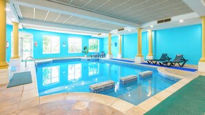 An indoor swimming pool with clear blue tiles, yellow columns, and sunlit windows.