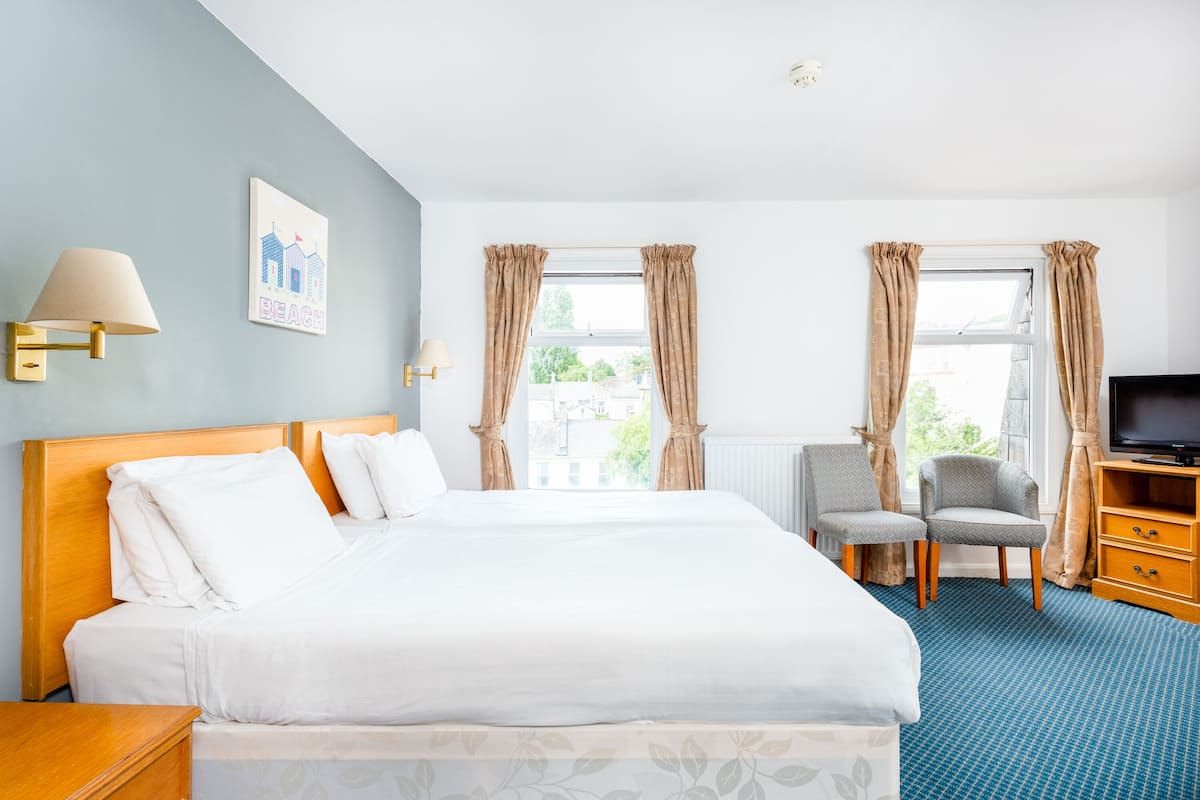 Ein Hotelzimmer mit einem großen Bett, zwei Stühlen, einem Fernseher und einem Fenster mit Vorhängen.