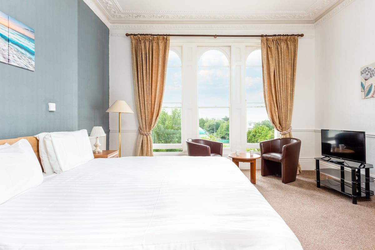 Ein Hotelzimmer mit einem großen Bett, einem Fernseher, einem Schreibtisch und einem Sessel.