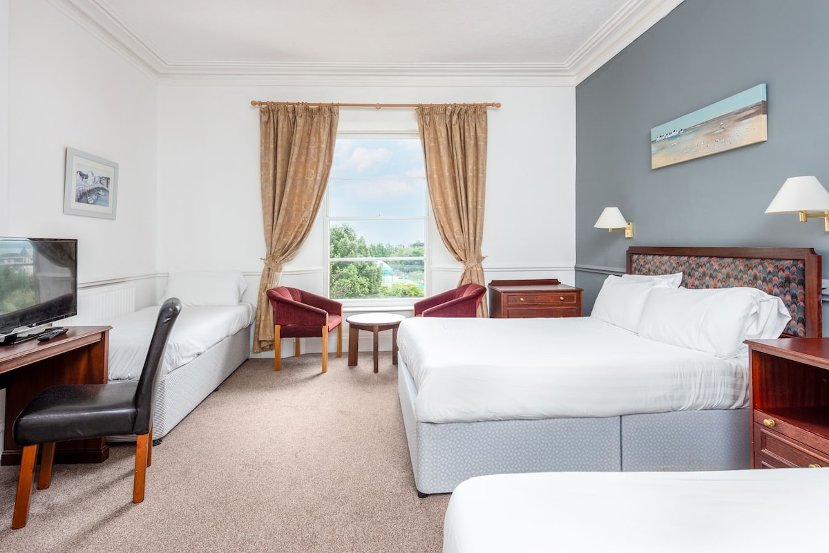 Ein Hotelzimmer mit einem Bett, einem Schreibtisch mit Stuhl, einem kleinen Tisch und zwei Sesseln.