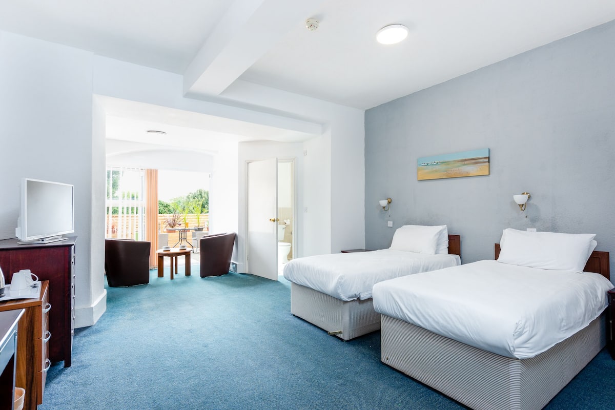 Ein Hotelzimmer mit zwei Betten, einem Schreibtisch mit Fernseher und einem Balkon mit Sitzgelegenheit.