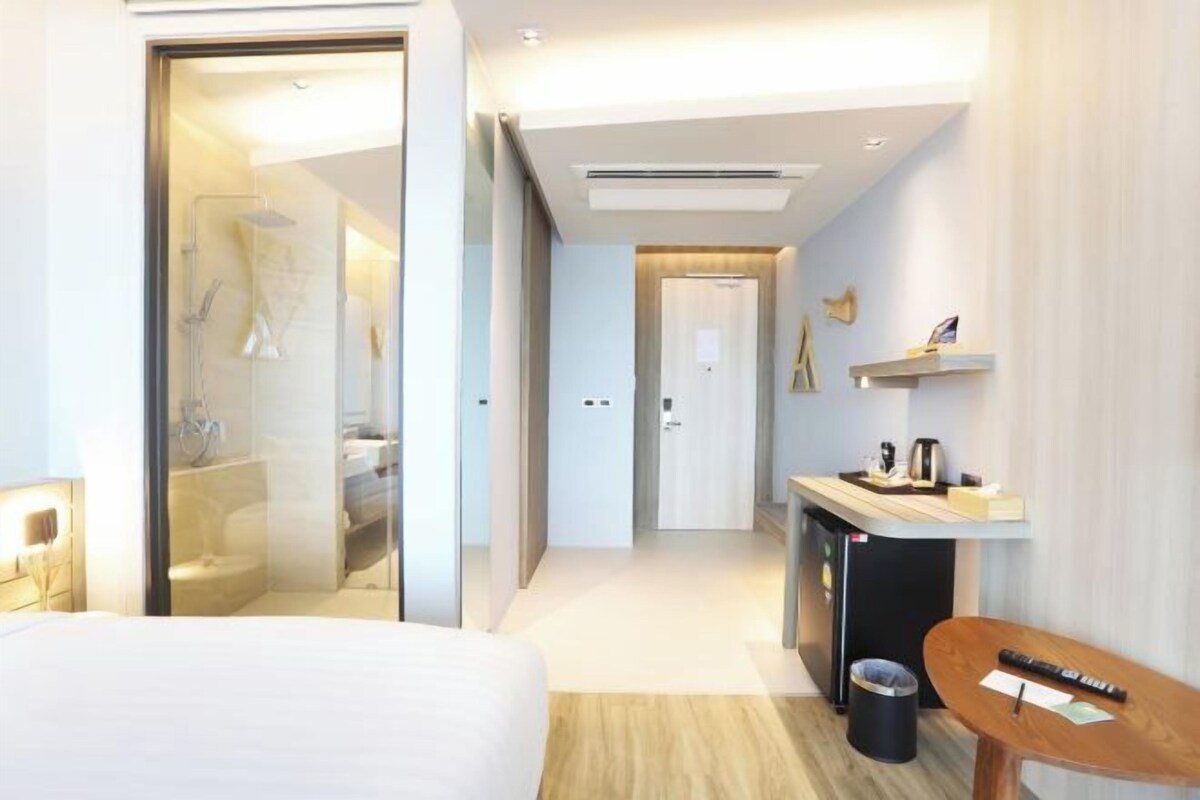 Ein modernes Hotelzimmer mit Bett, Schreibtisch, einer kleinen Mülltonne und einer Duschkabine.