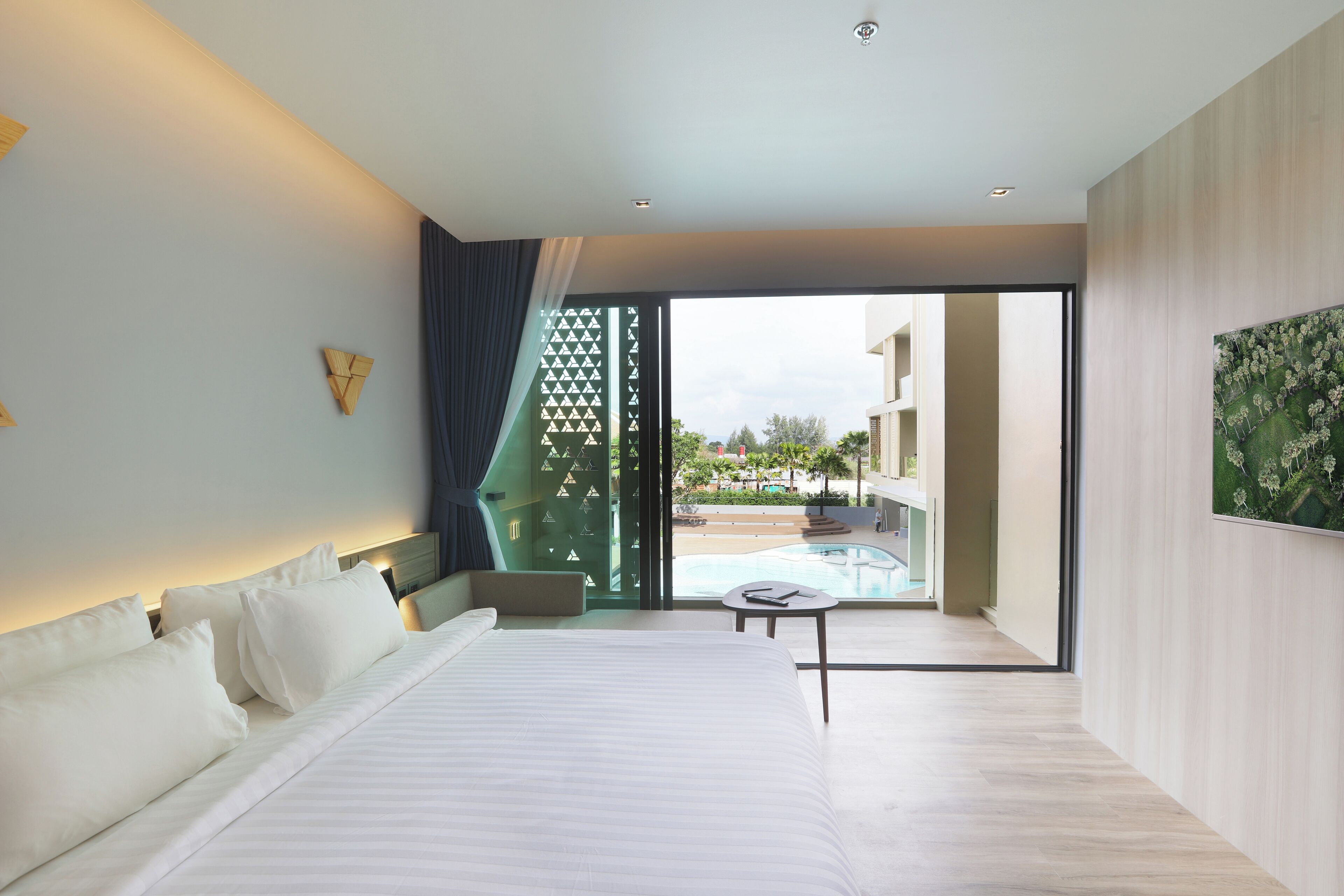 A modern hotel room with a large bed, a small table, and a view of a swimming pool and outdoor area.