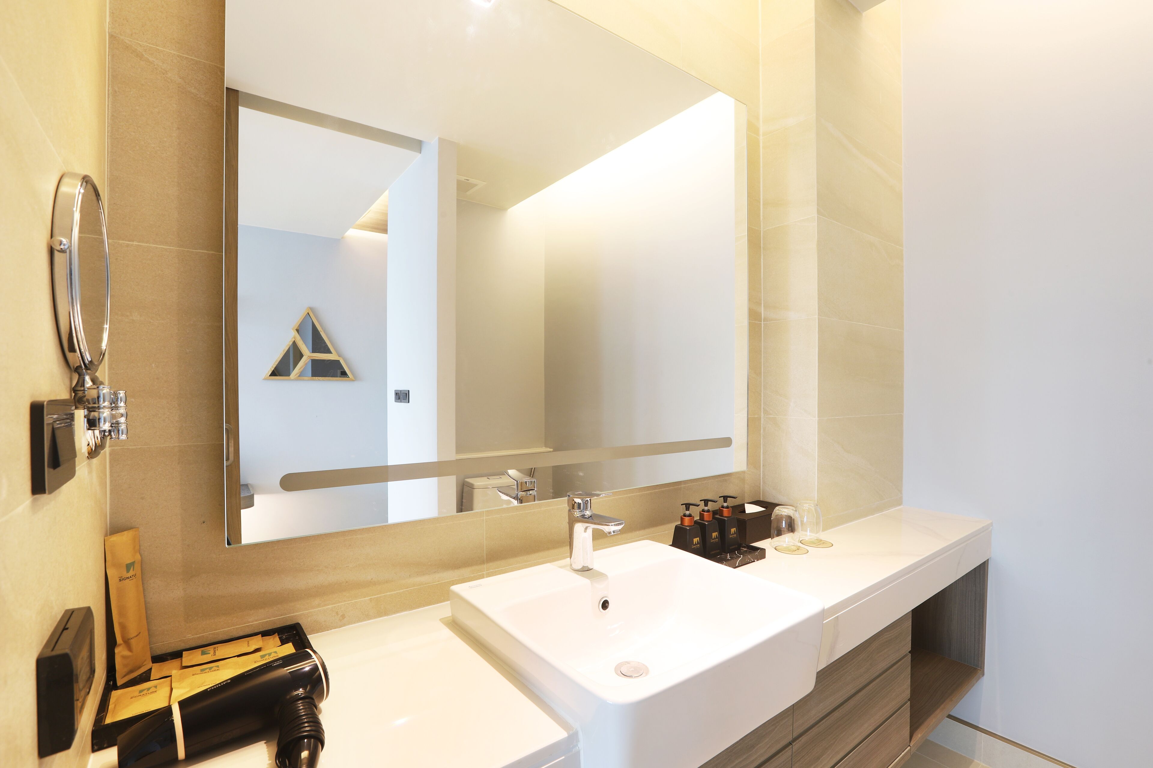 A modern bathroom with a large mirror, two sinks, and a vanity with storage.