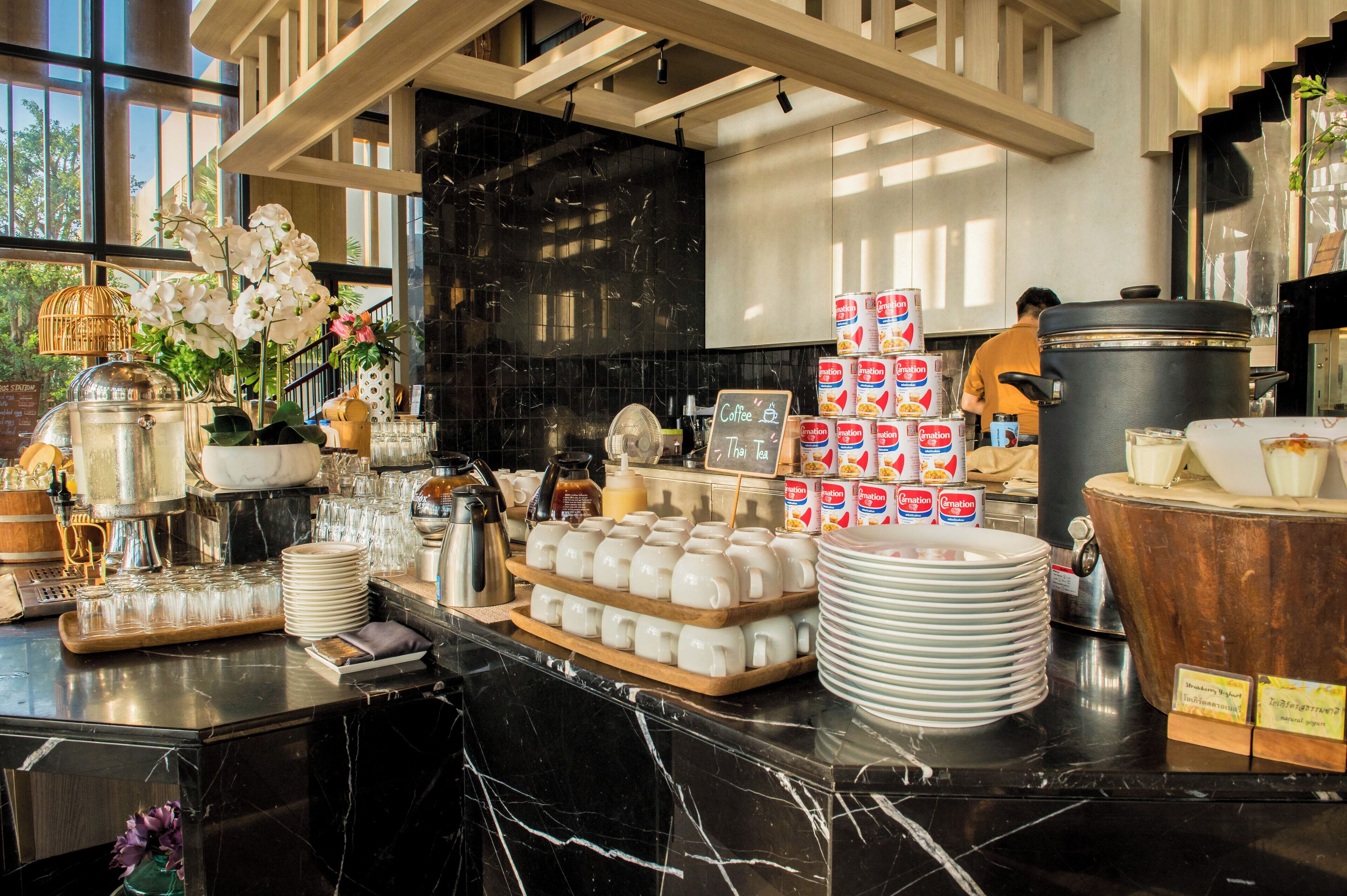 A coffee station with a variety of coffee-making equipment, including a coffee press, a scale, and multiple cups. There are also stacks of disposable cups and a large pot on the counter.