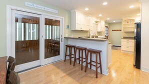 A kitchen with wooden flooring, white cabinets, and a black refrigerator. There are three wooden stools near the kitchen island.