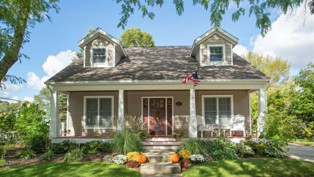 A two-story house with a front porch, a flag, and a mailbox.