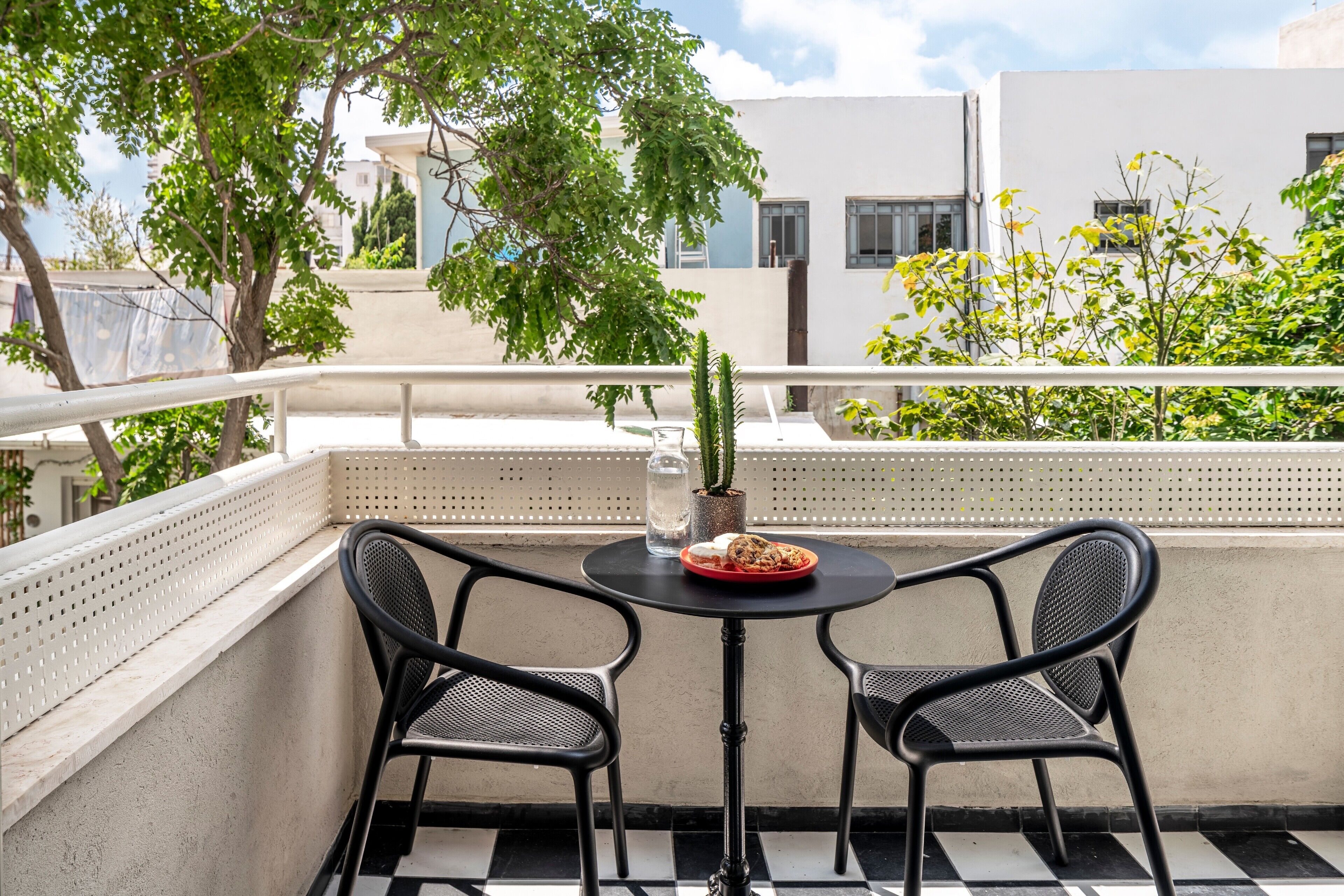 A balcony with two black metal chairs, a small round table, a potted cactus, and a red plate with food.