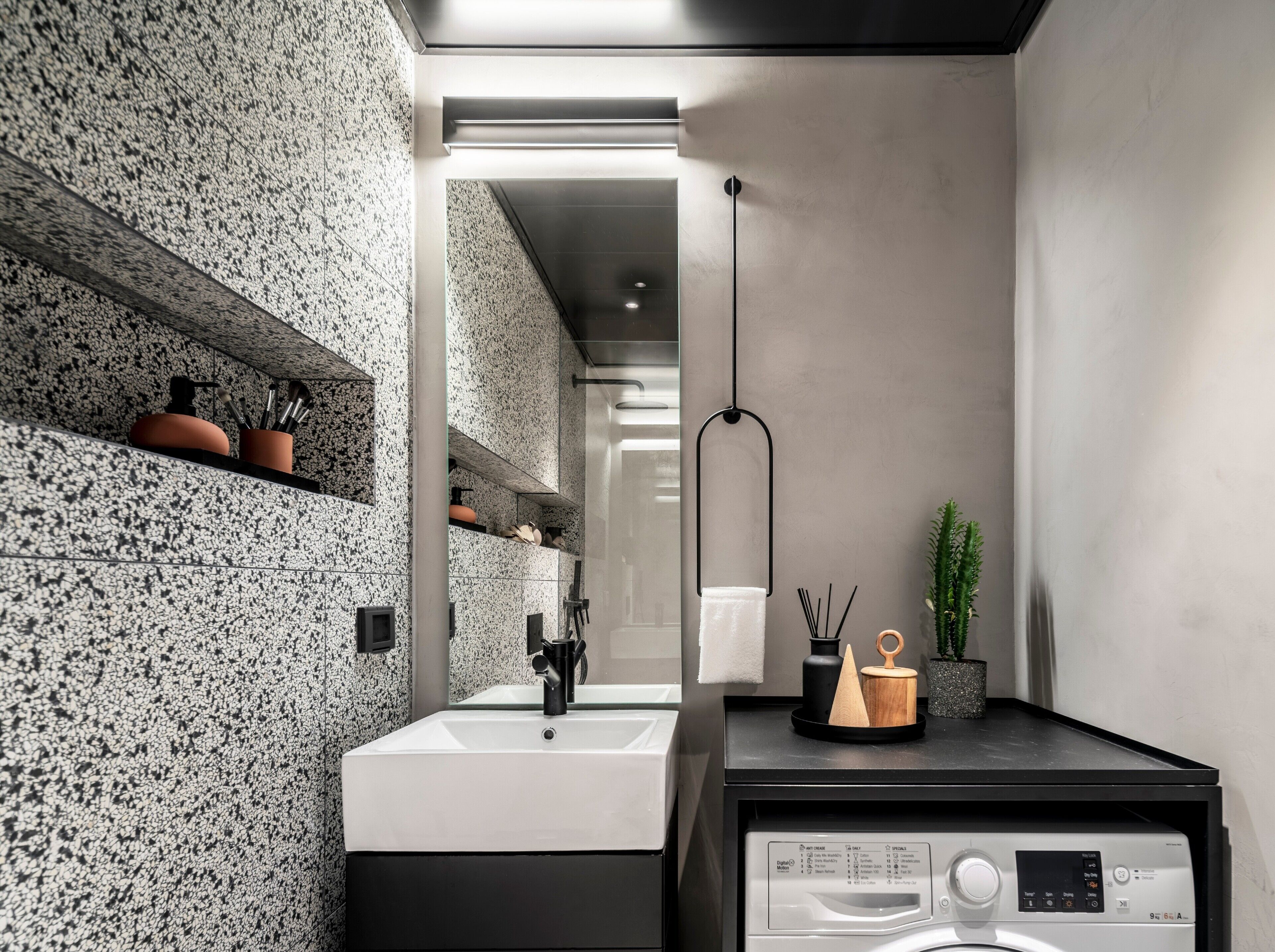 A modern bathroom with a granite backsplash, a white sink, a black countertop, a hanging light, and a washing machine.
