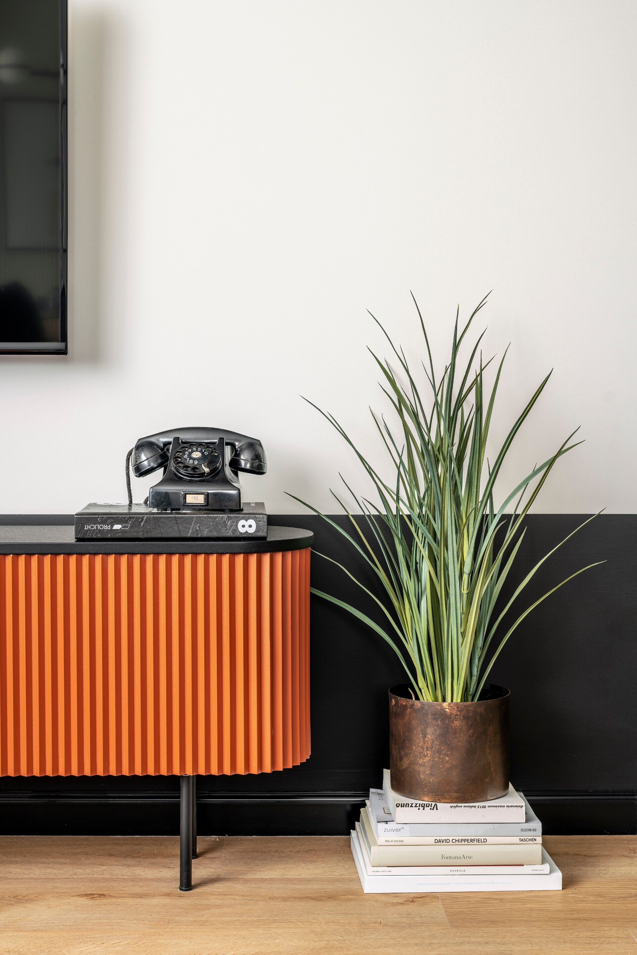 Una habitación moderna con un mueble negro y naranja, una planta en maceta y una pila de libros.