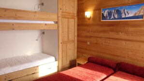 Ein Holzhüttenraum mit Etagenbett und Einzelbett, beide mit weißer Bettwäsche.