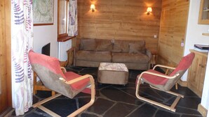 Ein gemütlicher Raum mit einer Holzwand, zwei Schaukelstühlen, einem Sofa und einem kleinen Tisch.